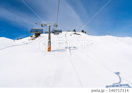Ski lift over snowy slopes in Saalbach Hinterglemm, Austria, during a bright winter ski day Ski lift over snowy slopes in Saalbach Hinterglemm, Austria, during a bright winter ski day 140717114