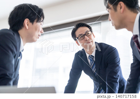 会議室で真剣に意見を交わすスーツ姿のビジネスマン3人 140717158