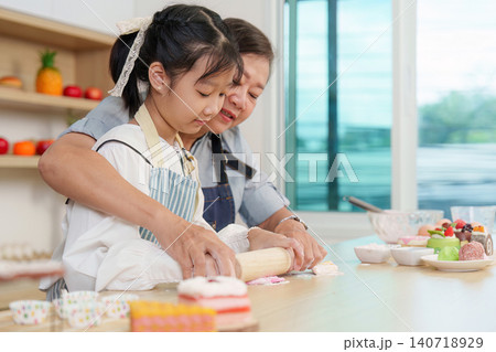 Asian grandmother teaching granddaughter to roll dough with rolling pin in kitchen Asian grandmother teaching granddaughter to roll dough with rolling pin in kitchen 140718929