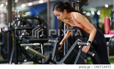 Asian woman exercising on row machine in gym for strength training Asian woman exercising on row machine in gym for strength training 140718955