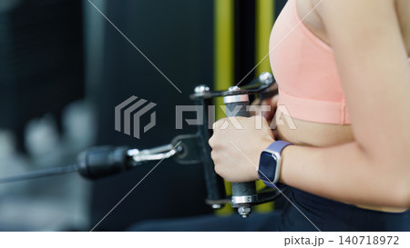 Cropped shot of woman pulling cable machine handle in gym for strength training Cropped shot of woman pulling cable machine handle in gym for strength training 140718972