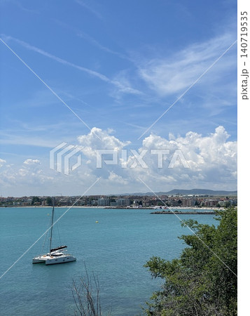 Sailboat on turquoise sea photo with coastal town, dramatic white clouds and blue sky, peaceful summer travel landscape for seaside vacation, tourism, sailing, nature and marine design 140719535