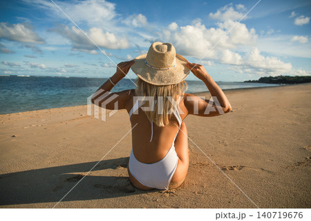 Woman sits on sandy beach looking at ocean and sky Woman sits on sandy beach looking at ocean and sky 140719676