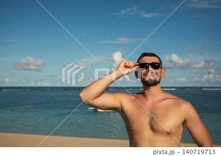 Man smiles while standing on a beach during summer time 140719713