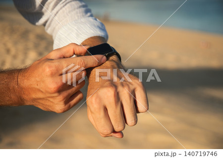 Man points at a watch on his wrist while on the sand 140719746