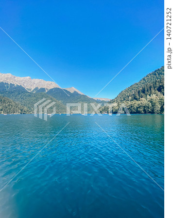 Crystal clear mountain lake surrounded by forested peaks under blue sky 140721252