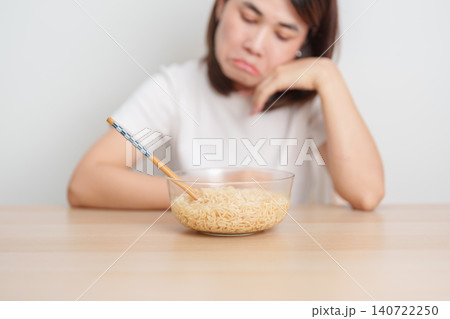Bored young Asian woman eating instant noodles at home. Exhausted female looking unhappy while eating bowl ramen. quick meal after work, burnout and unhealthy eating habit, lifestyle and cheap meal Bored young Asian woman eating instant noodles at home. Exhausted female looking unhappy while eating bowl ramen. quick meal after work, burnout and unhealthy eating habit, lifestyle and cheap meal 140722250