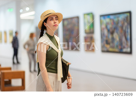 Mid shot of young pretty Caucasian woman in a straw hat and elegant clothes visits a contemporary art gallery. Copy space. Museum exhibition and cultural education Mid shot of young pretty Caucasian woman in a straw hat and elegant clothes visits a contemporary art gallery. Copy space. Museum exhibition and cultural education 140723609