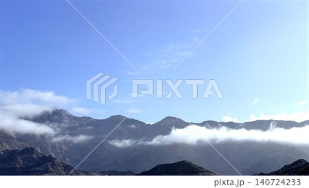 Mountain range with low clouds under clear blue sky 140724233