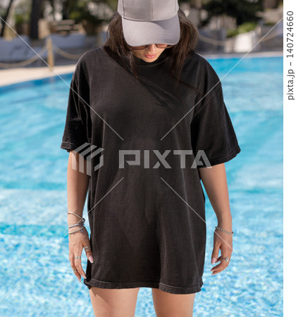 Blank washed black oversized t-shirt mockup, woman poolside at sunset, front view with copy space Blank washed black oversized t-shirt mockup, woman poolside at sunset, front view with copy space 140724660