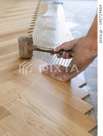 Worker installing herringbone parquet flooring with rubber mallet during hardwood floor installation 140724664