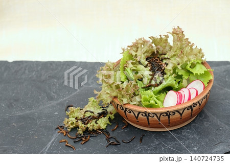 Edible mealworms lat. Tenebrio molitor and mixed fresh lettuce served in the bowl on stone table. 140724735