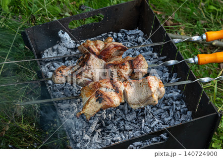 Grilling chicken skewers over hot coals at an outdoor gathering in a lush green setting during a sunny afternoon Grilling chicken skewers over hot coals at an outdoor gathering in a lush green setting during a sunny afternoon 140724900
