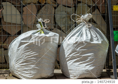 Two large white bags filled with gravel placed against a stone wall in daylight highlighting an outdoor construction work site Two large white bags filled with gravel placed against a stone wall in daylight highlighting an outdoor construction work site 140724910