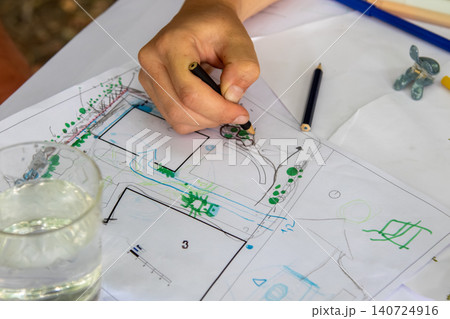 Hand drawing detailed landscape design on printed plan with colored pencils during outdoor planning session in natural setting Hand drawing detailed landscape design on printed plan with colored pencils during outdoor planning session in natural setting 140724916