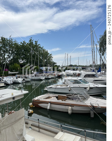 Scenic view of a busy harbor or yacht club under a bright blue sky with clouds. A variety of sailing yachts, motor boats Scenic view of a busy harbor or yacht club under a bright blue sky with clouds. A variety of sailing yachts, motor boats 140725176