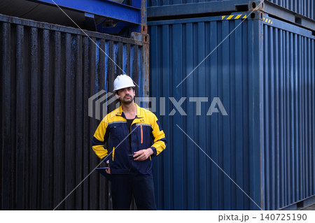 Logistics worker standing beside shipping containers at industrial freight terminal Logistics worker standing beside shipping containers at industrial freight terminal 140725190