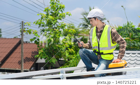 Solar Panel Installer Working on Rooftop with Drill and Toolbox in Residential Neighborhood 140725221