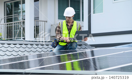 Solar Panel Technician Inspecting Rooftop Installation with Laptop on Residential Building 140725319