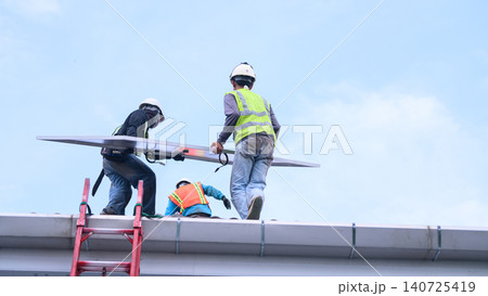 Workers Installing Solar Panel on Rooftop with Safety Gear and Hard Hats Against Blue Sky Workers Installing Solar Panel on Rooftop with Safety Gear and Hard Hats Against Blue Sky 140725419