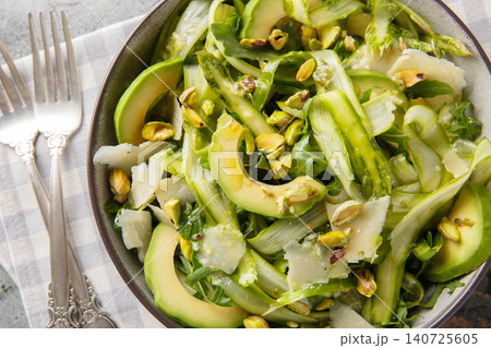 Elegant shaved asparagus parmesan salad with lemon dressing, pistachios, avocado, arugula closeup in the plate. Horizontal top view Elegant shaved asparagus parmesan salad with lemon dressing, pistachios, avocado, arugula closeup in the plate. Horizontal top view 140725605