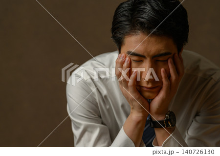 両手で頬杖をつくスーツ姿の男性 140726130