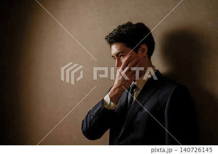 頬に手を当てて物思いにふけるスーツの男性 頬に手を当てて物思いにふけるスーツの男性 140726145