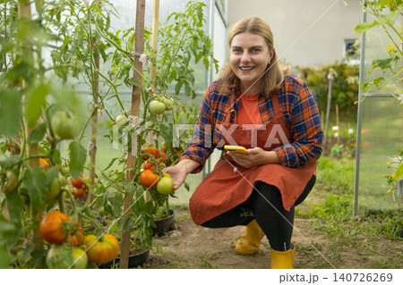Young woman farmer working with smartphone in greenhouse garden 140726269