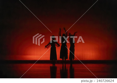Three female dancers performing a silhouette against red stage lighting Three female dancers performing a silhouette against red stage lighting 140726624