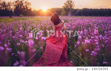 Young woman in long beautiful pink dress walks through blooming flower field. Spring and summer concept 140726705
