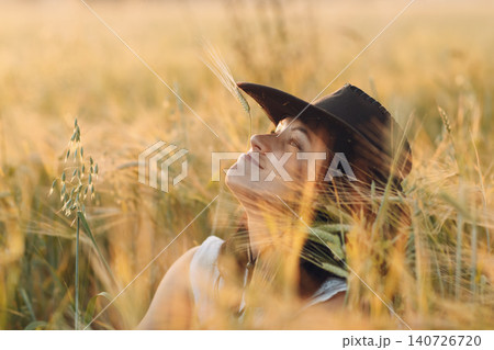 Woman farmer in cowboy hat at agricultural field on sunset. 140726720