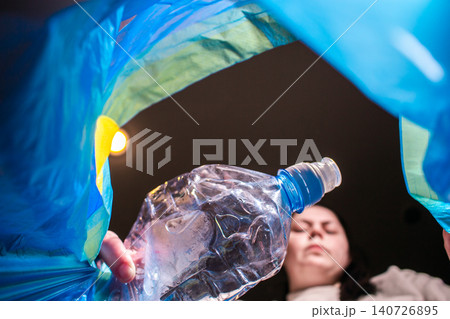 Woman throwing plastic bottle into blue trash bag. Low angle. Look from the inside of bag. High quality image Woman throwing plastic bottle into blue trash bag. Low angle. Look from the inside of bag. High quality image 140726895