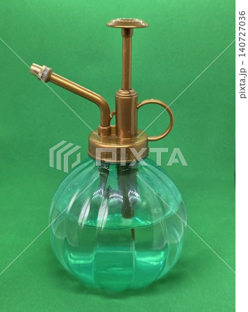 Vintage glass plant mister with brass pump isolated on green background. Gardening spray bottle for watering indoor plants, flowers and home care. Vintage glass plant mister with brass pump isolated on green background. Gardening spray bottle for watering indoor plants, flowers and home care. 140727036