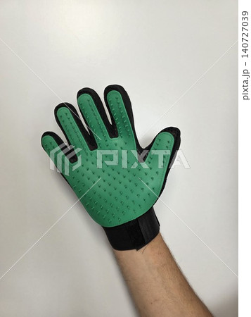 Green pet grooming glove on a human hand isolated on white background. Practical tool for removing loose fur, brushing cats and dogs, and everyday coat care. Green pet grooming glove on a human hand isolated on white background. Practical tool for removing loose fur, brushing cats and dogs, and everyday coat care. 140727039