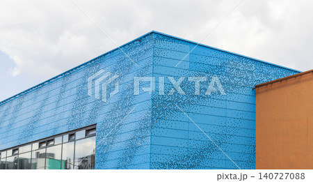 Modern building facade with bright blue perforated metal panels against cloudy sky. Urban Modern building facade with bright blue perforated metal panels against cloudy sky. Urban 140727088