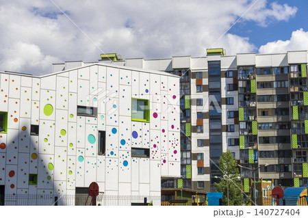 Modern kindergarten or school building with a playful colorful polka dot facade next to residential apartments 140727404