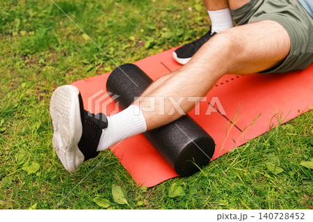 Close-up of a fit man performing myofascial release on a calf with a foam roller. Outdoor self-massage for muscle recovery, tension relief, and post-workout recovery. 140728452