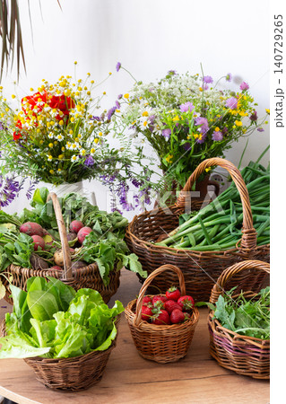 Freshly picked organic vegetables and strawberries are arranged in woven baskets on a wooden table. These local harvests show vibrant greens and red strawberries in a sunny setting Freshly picked organic vegetables and strawberries are arranged in woven baskets on a wooden table. These local harvests show vibrant greens and red strawberries in a sunny setting 140729265