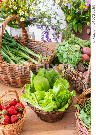 Freshly picked organic vegetables and strawberries are arranged in woven baskets on a wooden table. These local harvests show vibrant greens and red strawberries in a sunny setting Freshly picked organic vegetables and strawberries are arranged in woven baskets on a wooden table. These local harvests show vibrant greens and red strawberries in a sunny setting 140729269