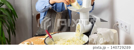 A 53-year-old man prepares cabbage and carrots for fermentation in his kitchen. He uses a machine to shred the vegetables while surrounded by kitchen tools and ingredients, banner A 53-year-old man prepares cabbage and carrots for fermentation in his kitchen. He uses a machine to shred the vegetables while surrounded by kitchen tools and ingredients, banner 140729289