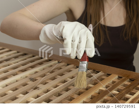 Woman brushes finish onto a wooden storage table. Close up of furniture care with gloves and a paintbrush. Home maintenance and wood restoration concept.. 140729591
