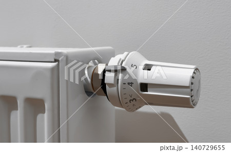 Thermostatic radiator valve on a white heater. Close up heating control in a home interior. Temperature regulation for energy saving and winter comfort.. 140729655