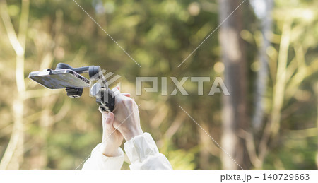 Smartphone on a handheld gimbal in a forest. Mobile filming gear for outdoor content creation. Nature background with travel and vlogging technology.. Smartphone on a handheld gimbal in a forest. Mobile filming gear for outdoor content creation. Nature background with travel and vlogging technology.. 140729663