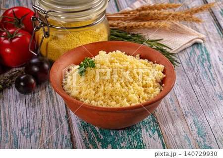 Cooked couscous in rustic clay bowl with fresh tomatoes and herbs on wooden table Cooked couscous in rustic clay bowl with fresh tomatoes and herbs on wooden table 140729930