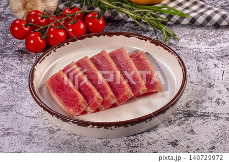 Raw sliced tuna steak on ceramic plate with fresh vegetables and herbs 140729972