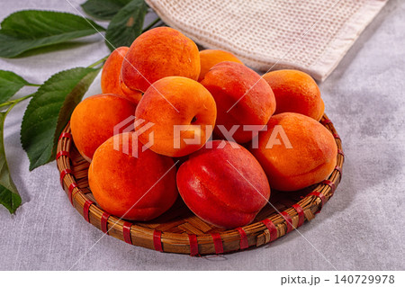 Fresh ripe apricots in woven basket with green leaves Fresh ripe apricots in woven basket with green leaves 140729978