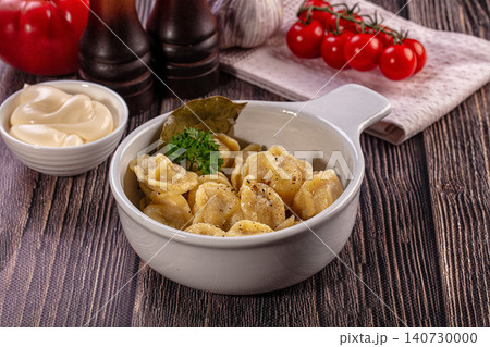 Bowl of boiled dumplings with sour cream and fresh vegetables on wooden table Bowl of boiled dumplings with sour cream and fresh vegetables on wooden table 140730000