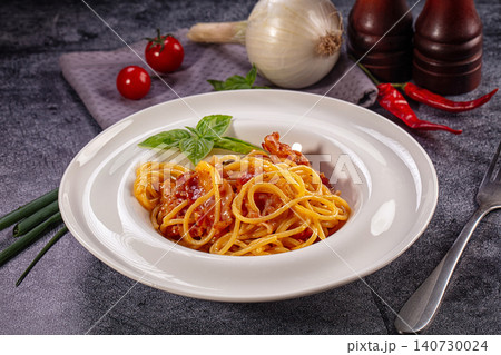 Spaghetti pasta with tomato sauce and bacon garnished with basil on dark stone table Spaghetti pasta with tomato sauce and bacon garnished with basil on dark stone table 140730024