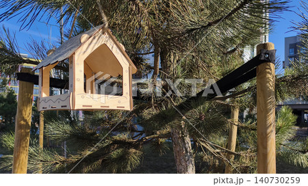 Wooden bird feeder mounted on support near tree in outdoor setting. Simple structure provides feeding place for wildlife in garden space. Concept of nature care habitat support.. 140730259