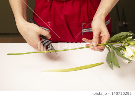 Florist cutting flower stems with pruning shears at table. Hands trimming plants preparing bouquet in workspace. Concept of floral arrangement process.. 140730293